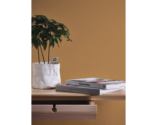 Dekorativ krukväxt i vit papperspåse bredvid böcker på ett nattduksbord