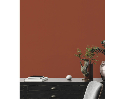 Dekorativ inredning med byrå, böcker, vas och krukväxter framför en vägg