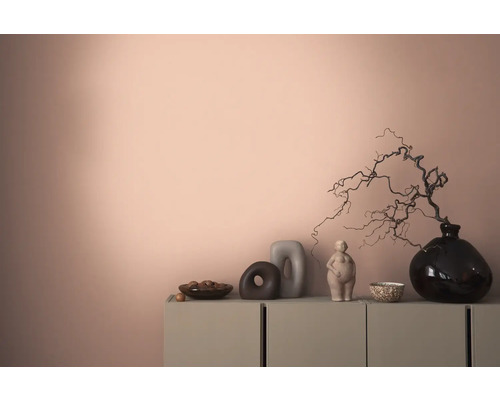 Dekorativ interiör med en byrå, vaser och skulpturer mot en färgad vägg.