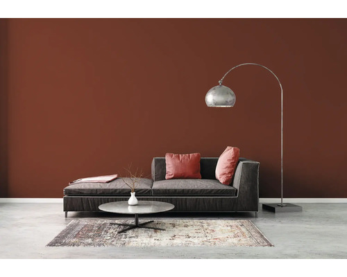 Vardagsrum med soffa, golvlampa och matta på betonggolv framför en brun vägg