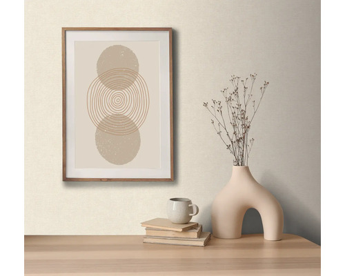 Dekorativt arrangemang med en inramad bild med abstrakt cirkelmotiv, en vas med torkade blommor, en kopp och böcker på ett bord.