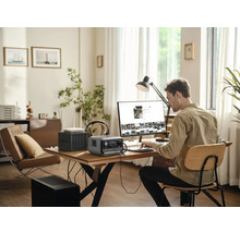 Man arbetar på en dator med en bärbar kraftstation, en router och en nätverkslagringsenhet på ett bord i ett ljust rum.