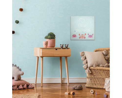 Barnrumsinredning med canvastavla, sidobord och rottingfåtölj.