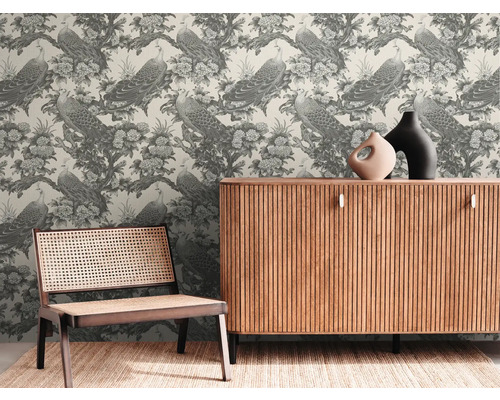 Dekorativt rum med tapeter med påfåglar och blommor, ett träskåp och en rottingstol.