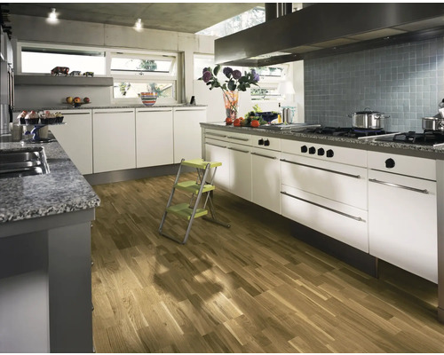 Ljust kök med vita skåp, bänkskiva i sten och trägolv.