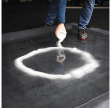 Person strör sand på en svart yta för att forma en cirkel.