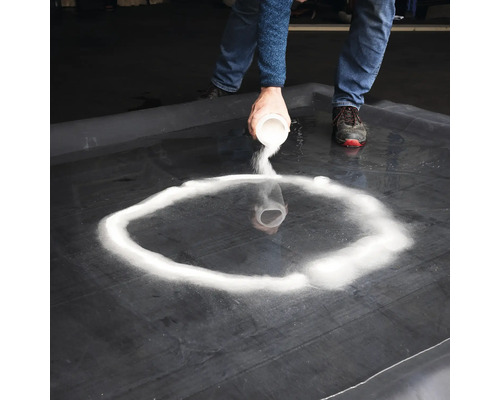 Person strör sand på en svart yta för att forma en cirkel.