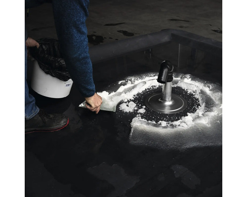 En person skottar en vit substans runt ett avlopp i en sopsäck.