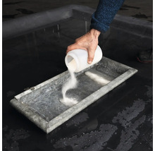 En person häller pulver från en behållare i ett tråg.