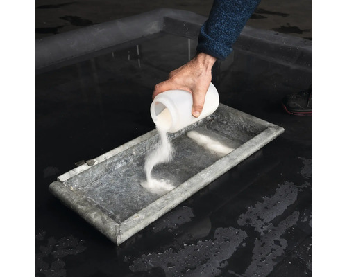 En person häller pulver från en behållare i ett tråg.