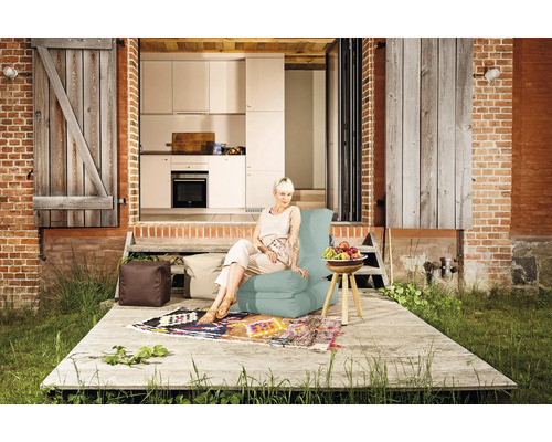 En kvinna sitter på en sittsäck på en terrass framför ett hus med öppet kök.