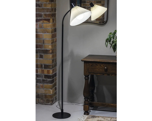 Golvlampa med plisserad lampskärm i ett vardagsrum bredvid en byrå.