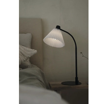 Dekorativ bordslampa med plisserad lampskärm på ett sängbord bredvid en säng.