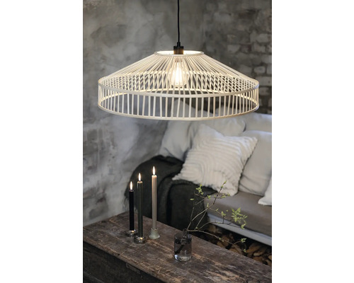 Dekorativ hänglampa av ljust trä ovanför ett träbord med ljus och dekoration, omgiven av en soffa med kuddar.