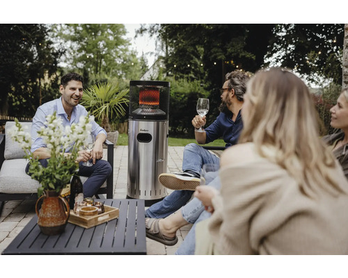 Grupp av människor sitter i trädgården med en Enders terrassvärmare i rostfritt stål, bord och blommor
