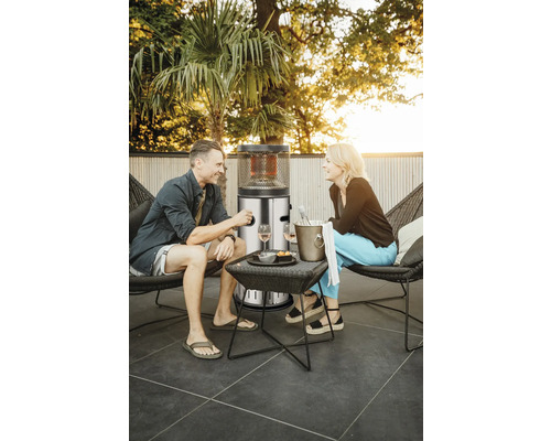 Scen med terrassvärmare, bord, två stolar och två personer utomhus.
