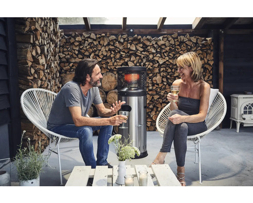 Terrass med man, kvinna, värmare, fåtöljer och vedförvaring