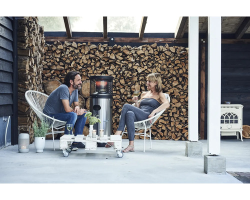 Scen med ett par som sitter i rottingstolar på en terrass, med en uteplatsvärmare, ett soffbord tillverkat av lastpallar och en hög med trä i bakgrunden