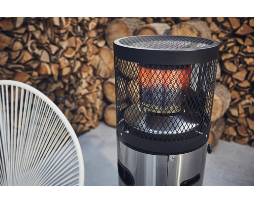 Terrassvärmare i rostfritt stål med skyddsgaller och stapel med ved i bakgrunden