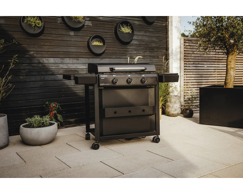 Svart gasolgrill med tre brännare och sidobord i utomhusmiljö.