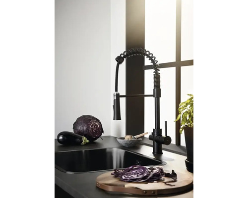 Svart köksblandare med grönsaker på en köksbänk framför ett fönster.