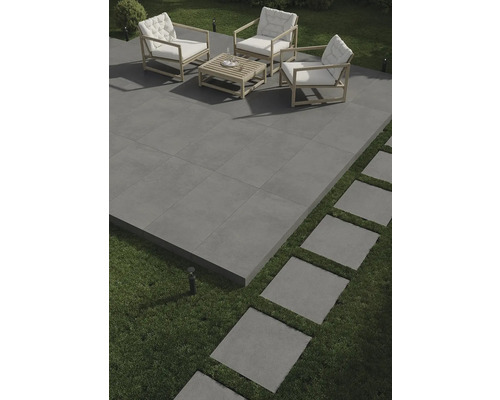 Terrass med grå plattor, sittgrupp med träram och vita kuddar samt trampstenar i gräsmattan.