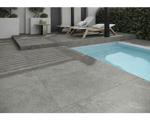 Grå terrassplattor bredvid en pool med solstolar