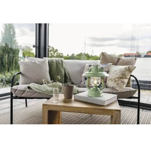 Dekorativ vardagsrumsscen med soffa, kuddar, filt, bord, lampa, mugg och vas med blommor.