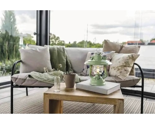 Dekorativ vardagsrumsscen med soffa, kuddar, filt, bord, lampa, mugg och vas med blommor.