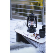 Stilleben med fotogenlampa, handskar och drycker på ett bord utomhus.