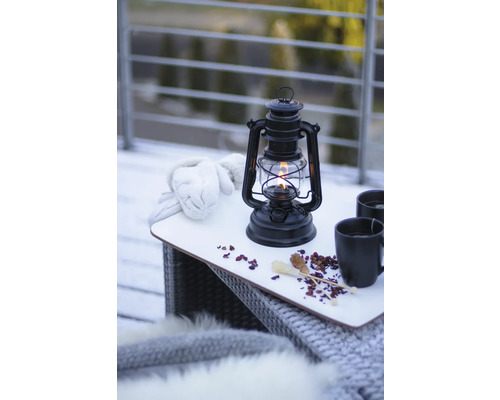Stilleben med fotogenlampa, handskar och drycker på ett bord utomhus.