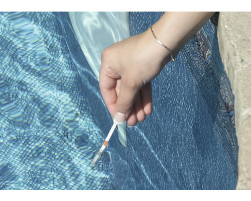 En person testar poolvattnet med en testremsa