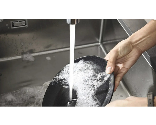 En person diskar en stekpanna i en diskho under rinnande vatten.