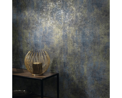 Närbild av en strukturtapet med ett abstrakt mönster i dämpade färger och en gyllene ljusstake