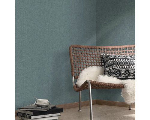 Vardagsrumsscen med rottingstol, kudde och mönstrad tapet.