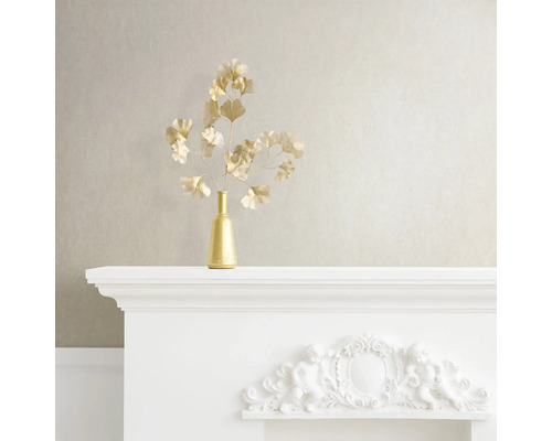 Dekorativt stilleben med gyllene vas och ginkgogrenar på en vit spiselkrans.