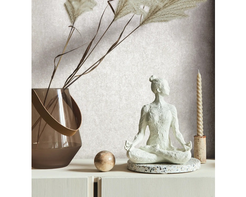 Dekorativ scen med en yogafigur, en vas med prydnadsgräs, en boll och ett ljus på en vit byrå.