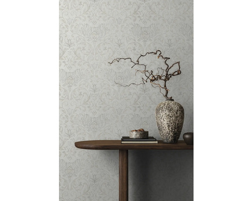 Detaljvy av en dekorerad vägg med blommönstrad tapet, ett träbord med dekorationer och en vas med grenar.