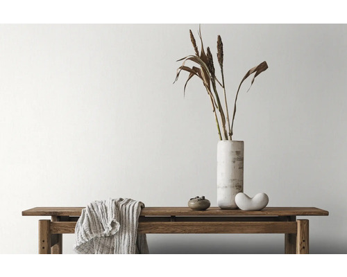 Dekorativt arrangemang med bänk, vas, prydnadsgräs och textilier inomhus.