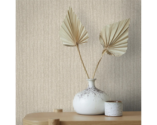 Närbild av en vägg med tapet med stickat mönster, dekorerad med en vas och torkade palmblad på ett träbord.