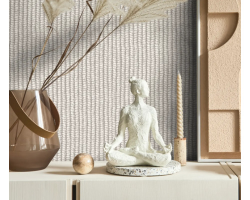 Dekorativt rum med stickad tapet, en Buddha-staty, en vas med torkade blommor och ett ljus.
