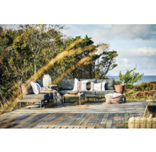 En utomhusscen med loungemöbler, bestående av soffa, fåtölj och bord, på en träterrass framför träd och havet.