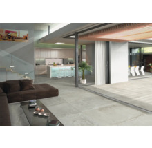 Ljust vardagsrum med betongliknande golvplattor, soffa och öppet kök