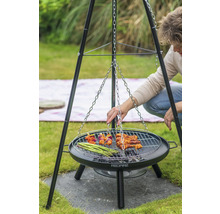 Person grillar på en trebensgrill med ett grillgaller som en kedja är fäst vid. På gallret ligger spett, kött och grön sparris.