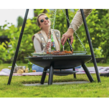 Person grillar kött på en trebensgrill i trädgården