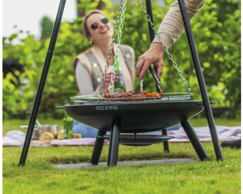 Person grillar kött på en trebensgrill i trädgården