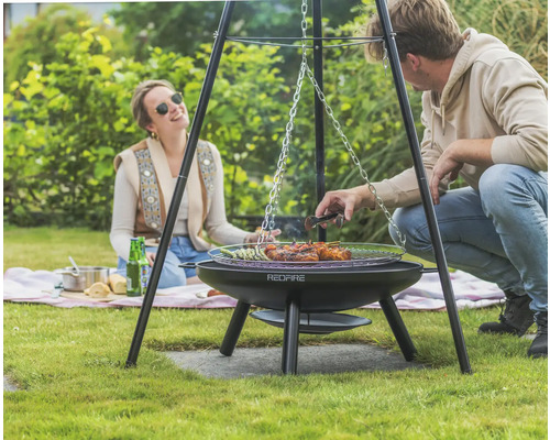 Scen med en Redfire trebensgrill i trädgården med två personer som grillar mat.