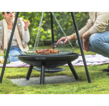 Tre personer grillar kött och grönsaker på en trebensgrill i trädgården.