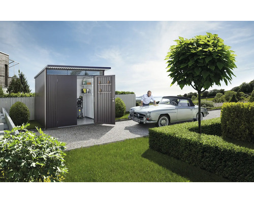 Rymligt redskapsbod i metall med öppen dörr i en trädgård och man putsar veteranbil
