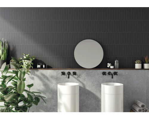 Badrum med mörka väggplattor, två handfat, rund spegel och dekoration